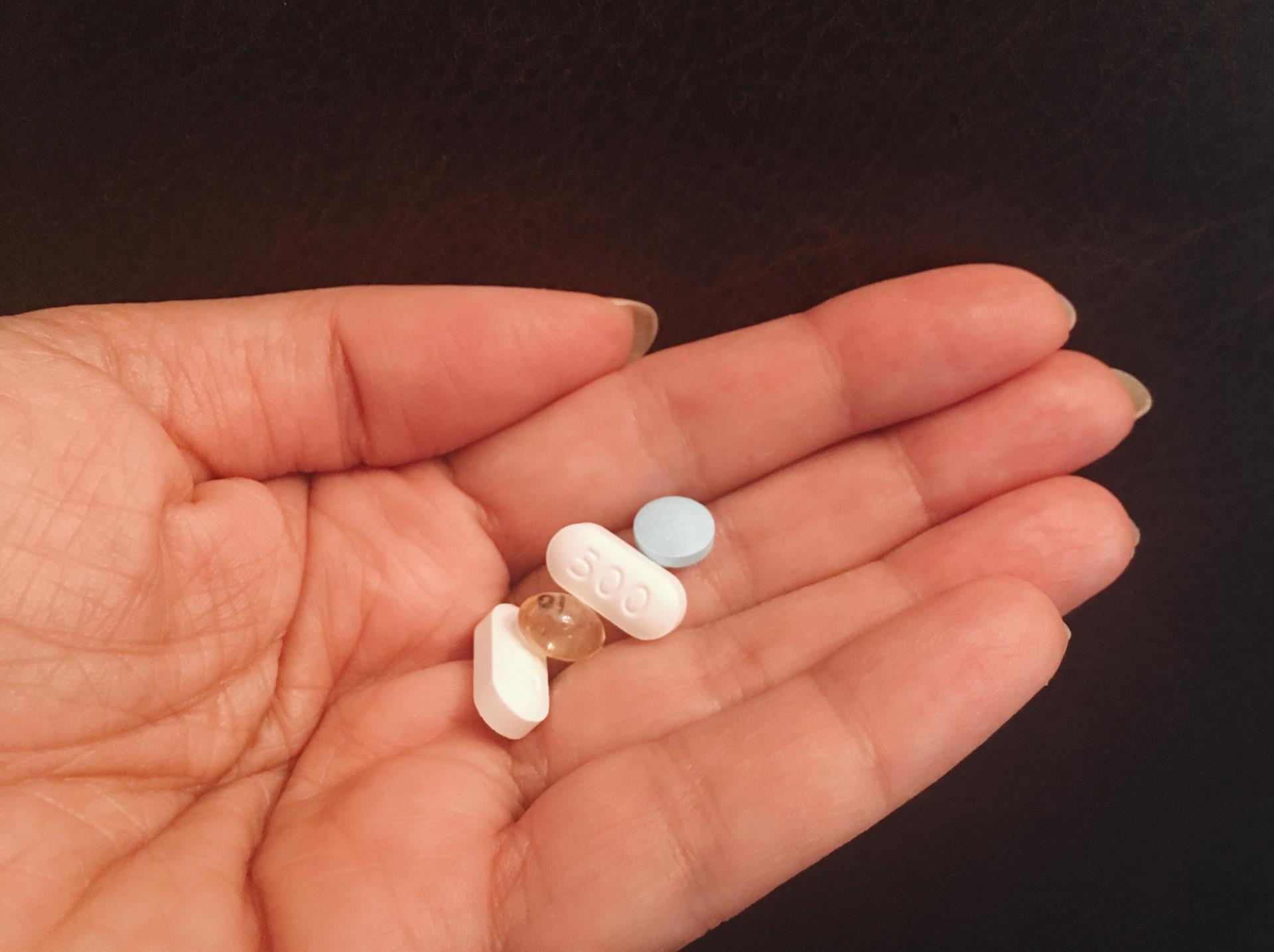 A hand holding four different tablets and capsules