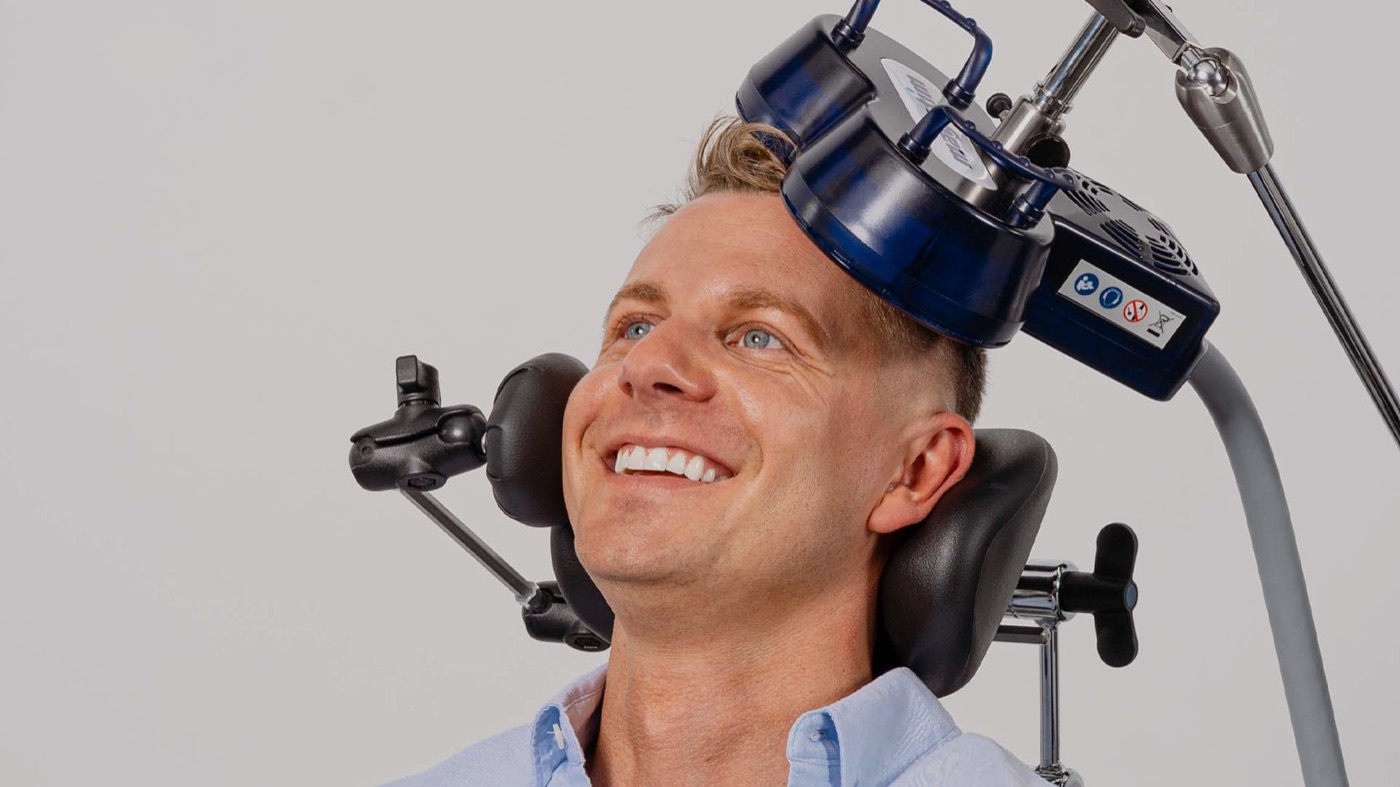 A smiling patient seated with the Magstim treatment coil positioned against the side of his head